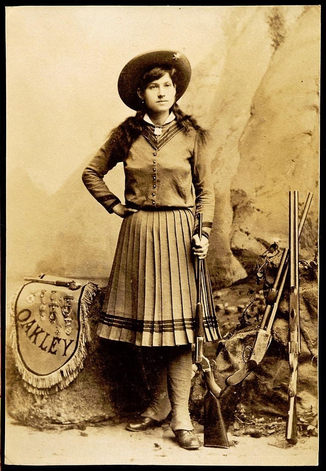 A publicity still of Annie Oakley loading a shotgun.