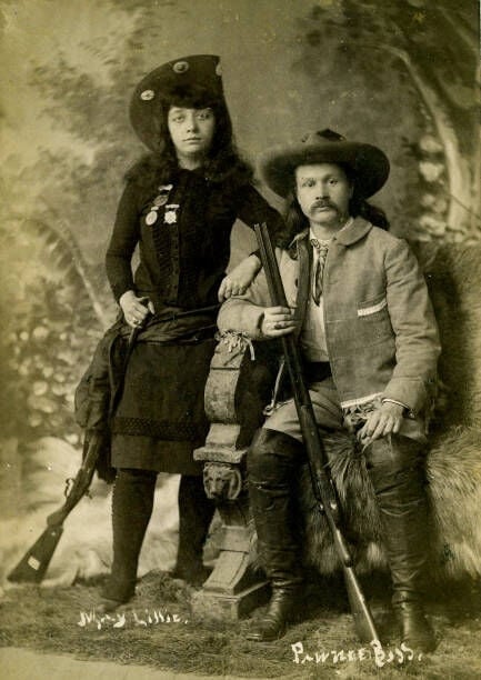 Wild West Photo Of Gordon Lillie (Pawnee Bill) & May Lillie, Circa 1890S. May Lillie Is Standing In Her Wild West Outfit Displaying Her Medals, A Great Cowgirl Hat, And Her Rifle. Gordon Is Sitting In His Knee High Boots, Wild West Jacket, Great Cowboy Hat, And Holding A Double Barrel Shotgun. Wild West Photo Of Gordon Lillie (Pawnee Bill) & May Lillie,. (Photo by Swords Brothers/Buyenlarge/Getty Images)