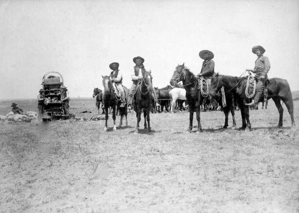 Great Image Of Cowboys At Round-Up On The 3-C Ranch Four Cowboys On Horseback Watching Over A Group Of Nearby Ponies. Two Men Work The Chuck Wagon As Another Cowboy Reclines Amid Bed Rolls And Bagged Supplies. (Photo by Buyenlarge/Getty Images)