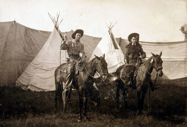 Wild West Female Performer May Mackey 1890-1900. Two Wild West Performers May Mackey And Unidentified Wild West Male (Cowboy) Performer Are On Horses In Front Of Two Teepees At A Wild West Show. Both Performers Have Wild West Gear: Guns, Lassoes, And Gauntlets And Cowboy Hats. (Photo by Buyenlarge/Getty Images)