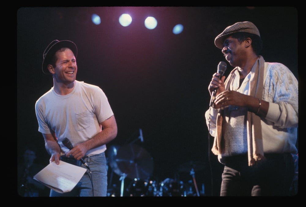 (Original Caption) : 1987: Actor Bruce Willis laughs while singing on stage with musician Ben E. King.   (Photo by Lynn Goldsmith/Corbis/VCG via Getty Images)