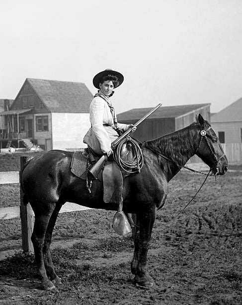 A young woman sits side saddle astride a horse while holding a double barrel shotgun. (Photo by Kirn Vintage Stock/Corbis via Getty Images)